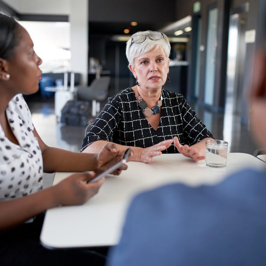 Unposed shot of senior businesswoman managing team of diverse mixed race professional male anf female office colleagues in large bright conference room with tablet